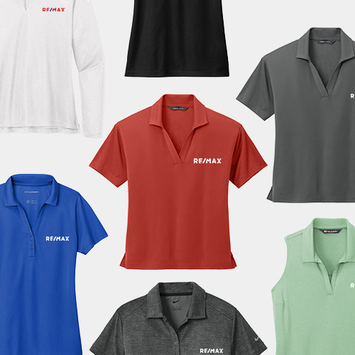 A collection of six polo shirts in various colors, each with the RE/MAX logo prominently displayed on the front. From top to bottom and left to right: the first row shows a white polo with the logo on the left chest, a black polo, and a dark grey polo, all with collars and a few buttons below the collar. The second row shows a bright blue polo and a brick red polo with the RE/MAX logo across the chest, and a light green polo with the logo on the left chest. The third row displays a charcoal grey polo with the RE/MAX logo across the chest. Each shirt is neatly laid out and the image is set against a white background.